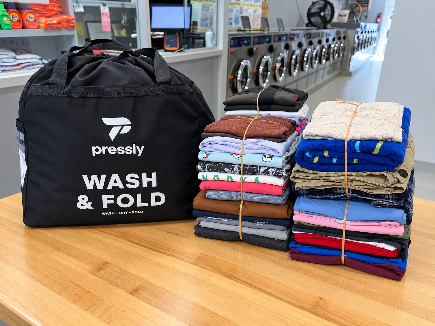 A Pressly wash and fold bag beside two stacks of folded laundry